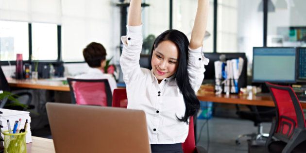 asian businesswoman stretching arms in the air to celebrate completion of task.
