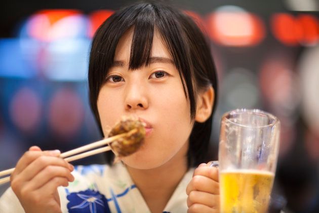 ビールを片手にたこ焼きを食べる女性のイメージ写真