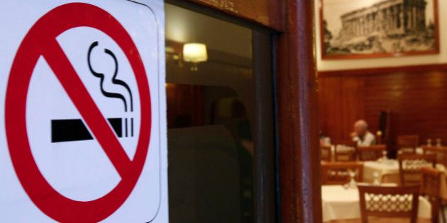 A man eats behind a smoking ban sign in a restaurant-cafe in central Athens, October 18, 2010. Businesses around Greece have decided to violate a smoking ban and have placed ashtrays back on tables and allow customers to smoke inside, despite the law and heavy fines, saying an economic crisis and smoking ban simultaneously is killing business. REUTERS/John Kolesidis (Greece - Tags: POLITICS SOCIETY BUSINESS)
