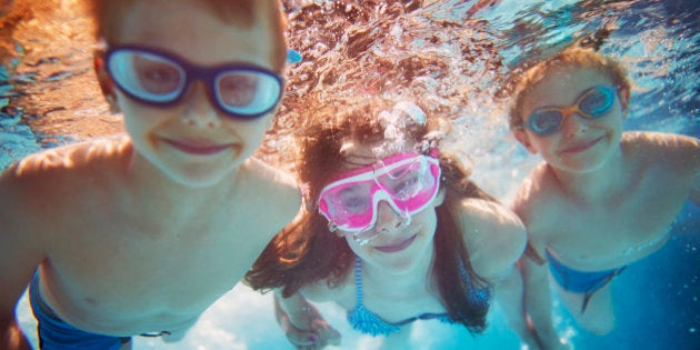 Three kids swimming underwater. Little girl and her brothers having fun in the swimming pool. Focus in the little girl, brothers are out of focus.