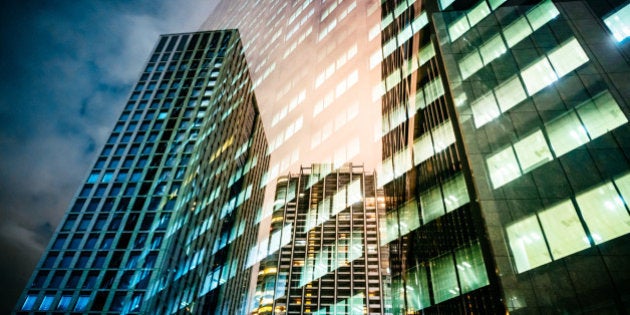 Dramatic sky and corporate architecture reflecting at night in glass.