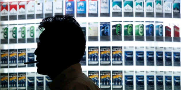 A man smokes a cigarette in front of a cigarettes store displaying several packages of brands in Tokyo August 25, 2014. REUTERS/Issei Kato (JAPAN - Tags: SOCIETY)