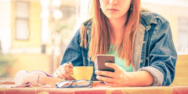 Vintage filtered portrait of serious pensive young woman with smartphone - Hipster girl using mobile smart phone while drinking coffee - Concept of human emotions - Soft focus on sad worried face
