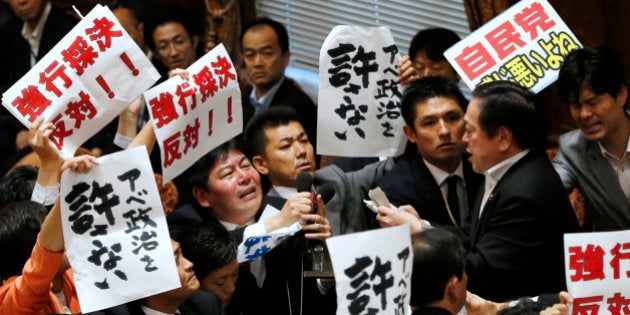 Opposition lawmakers surround Yasukazu Hamada, right, chairman of the lower house special committee on security legislation, as Hamada continues the committee proceedings at the parliament in Tokyo, Wednesday, July 15, 2015. The parliamentary committee has approved a package of highly controversial security legislation in a vote forced by Prime Minister Shinzo Abeâs ruling bloc disrupted by opponents' massive protests. The banners held by opposition lawmakers read