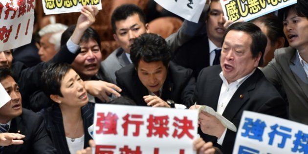 Yasukazu Hamada (2nd R), chairman of a parliamentary panel on Japanese Prime Minister Shinzo Abe's controversial security bills, is surrounded by opposition lawmakers holding placards which say 'Opposed to forced passage of the bills', during a parliamentary committee discussion on the bills at the National Diet in Tokyo on July 15, 2015. Abe made another pitch on July 15 for security bills which would beef up Japan's military, as he pushed legislation through a key panel despite surging public and parliamentary opposition. The controversial bills that would expand the remit of the country's armed forces were approved by the lawmakers of the ruling coalition. AFP PHOTO / Yoshikazu TSUNO (Photo credit should read YOSHIKAZU TSUNO/AFP/Getty Images)