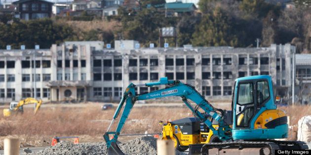 An excavator operates on a construction site as an abandoned elementary school stands in the background in an area damaged by the tsunami following the Great East Japan Earthquake in Ishinomaki, Miyagi Prefecture, Japan, on Sunday, March 10, 2013. Japan's economy grew at an annualized 0.2 percent last quarter after shrinking 3.7 percent the three previous months, the worst since the 2011 earthquake, revised government data show. Photographer: Kiyoshi Ota/Bloomberg via Getty Images