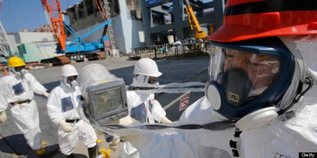 A radiation monitor reads 114.00 microsieverts per hour as members of the media and Tokyo Electric Power Co. (Tepco) employees, wearing protective suits and masks, visit the No. 4 reactor building, background center, and the construction of a storage unit for melted fuel rods, background right, at the company's Fukushima Dai-Ichi nuclear power plant in Okuma, Fukushima Prefecture, Japan, on Wednesday, March 6, 2013. Tepco's Fukushima Dai-Ichi plant had three reactor core meltdowns after it was hit by an earthquake and tsunami on March 11, 2011. Photographer: Issei Kato/Pool via Bloomberg