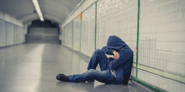 Young man abandoned lost in depression sitting on ground street subway tunnel suffering emotional pain, sadness and looking destroyed and desperate leaning on wall alone