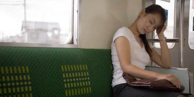 Young woman sitting on train holding bag on lap, eyes closed
