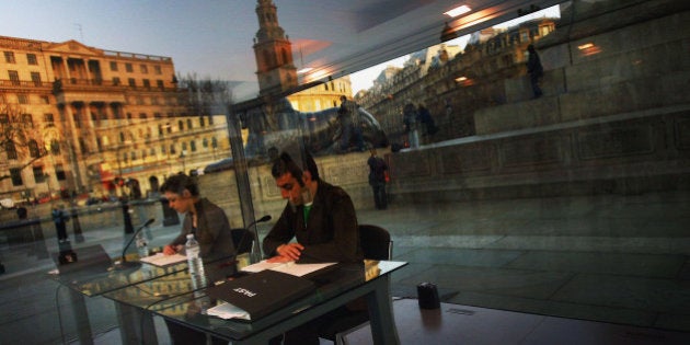 LONDON - MARCH 30: Onlookers marvel at the 'Reading One Million Years' art installation by Japanist artist On Kawarain on March 30, 2004 in Trafalgar Square, London. For seven hours a day from 8am yesterday, several pairs of men and women will sit in this box and read from two printed lists of years from 998,031BC to AD1969 - the year Kawara conceived the idea - and AD1980 to AD 1,001,980. Working flat out, it is predicted the British team will only read around 217,000 years. (Photo by Bruno Vincent/Getty Images) *** Local Caption ***