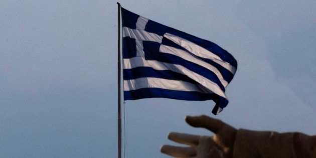 A hand of a statue is seen as the Greek flag waves in Athens, Sunday, June 28, 2015. Greek Prime Minister Alexis Tsipras says the Bank of Greece has recommended that banks remain closed and restrictions be imposed on transactions, after the European Central Bank didn't increase the amount of emergency liquidity the lenders can access from the central bank. (AP Photo/Daniel Ochoa de Olza)