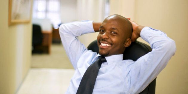 Businessman relaxes in a chair with hands behind his head in an office. Pretoria, South Africa