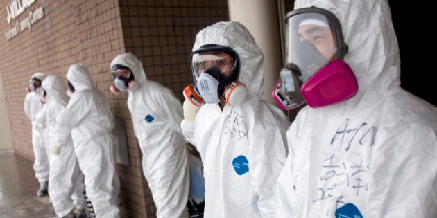 Workers dressed in protective suits and masks wait outside a building at J-Village, a soccer training complex now serving as an operation base for those battling Japan's nuclear disaster, in Fukushima, Japan, on Friday, Nov. 11, 2011. Tokyo Electric Power Co. is struggling to contain the worst nuclear disaster in 25 years. Photographer: David Guttenfelder/Pool via Bloomberg via Getty Images