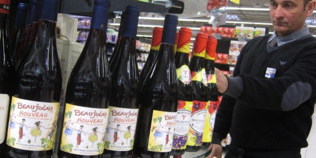 A shop assistant at a store in Nice, southeastern France, arranges bottles of 2013 Beaujolais Nouveau, Thursday, Nov. 21, 2013. According to French law, the wine is released on the third Thursday of each November and this year's theme celebrates the spirit of the roaring 1920's. Beaujolais Nouveau is easy to drink, but everything a fine wine is not: young, poor in tannins and not suited to storage. It's partially because new wines could never hope to stir the imagination the way that the great wines of Bordeaux or Champagne do that the makers of Beaujolais Nouveau resorted to what has become a hugely successful marketing campaign. (AP Photo/Lionel Cironneau)