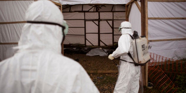 In this photo taken on Wednesday, Sept. 24, 2014, healthcare workers spray disinfectant as they enter a makeshift morgue with the bodies of people suspecting of dying from the Ebola virus, in Kenema, Sierra Leone, Thursday, Sept. 25, 2014. Sierra Leone restricted travel Thursday, Sept. 25, 2014 in three more