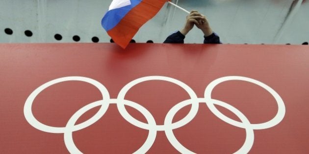 FILE - In this Feb. 18, 2014 file photo, a Russian skating fan holds the country's national flag over the Olympic rings before the start of the men's 10,000-meter speedskating race at Adler Arena Skating Center during the 2014 Winter Olympics in Sochi, Russia. The IOC's ruling 15-member executive board will meet Sunday, July 24, 2016 via teleconference to weigh the unprecedented step of excluding Russia as a whole from the 2016 Rio Olympic Games because of systematic, state-sponsored cheating. (AP Photo/David J. Phillip, file)