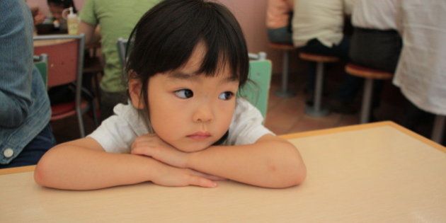 Sad girl sitting on chair leaning on table, Japan.