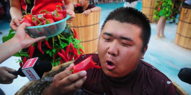 HANGZHOU, CHINA - JULY 20: A man sitting in an ice bucket eats peppers during a competition at Song Dynasty Town on July 20, 2016 in Hangzhou, Zhejiang Province of China. As the ground temperature reached 40 degrees Celsius in Hangzhou, tourists competed eating peppers while sitting in the ice buckets to feel hot and cool at the same time in the Song Dynasty Town scenic area. (Photo by VCG/VCG via Getty Images)