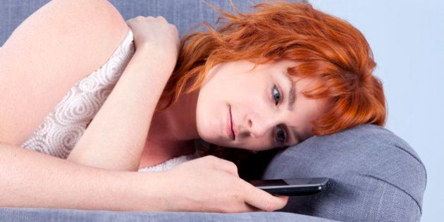 Close-up of a cute young redhead lying on a sofa whilst texting.