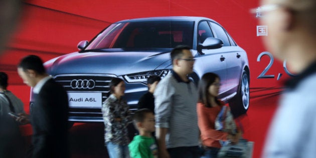 Visitors walk past an advertisement for the Audi A6L sedan manufactured by FAW Audi, the joint venture...