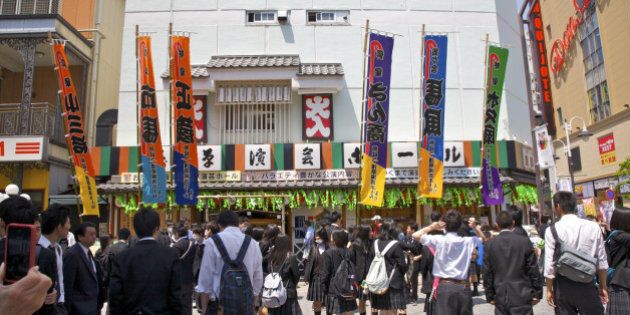 Adults and uniformed schoolchildren standing outside historic Asakusa Entertainment Hall, Asakusa, Tokyo, Japan. This pop entertainment hall offers Rakugo (comic storytelling), Manzai (comic dialogue), Mandan (comic monologue), acrobatics, magic and mimic shows.