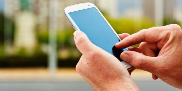 In a city street, a man's hands touch the blank screen on a modern cellphone with an android operating system. The blank screen offers copy space for your message.