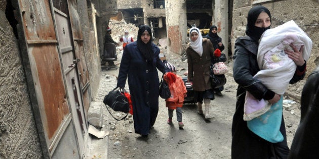 FILE - In this Feb. 4, 2014, file photo released by the Syrian official news agency SANA, residents of the besieged Yarmouk Palestinian refugee camp carry their belongings as they flee the camp, on the southern edge of the Syrian capital Damascus, Syria. Conditions in the camp have deteriorated since Islamic State militants muscled their way into it in early April 2015. The militants are trying to consolidate their hold on the camp. (AP Photo/SANA, File)