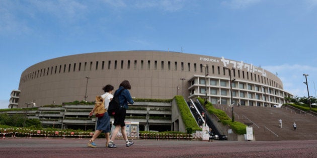 Pedestrians walk past the Yahuoku! Dome, operated by Fukuoka SoftBank Hawks Corp., in Fukuoka, Japan, on Saturday, July 18, 2015. Prices of many products will need to rise at a faster rate than the goal to make up for a drag on the inflation index from distorted housing costs in the gauge, Kiyohiko Nishimura, 62, who heads a government statistics panel, said on July 15. Photographer: Akio Kon/Bloomberg via Getty Images