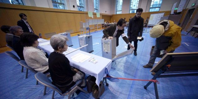 A representative of a local election administration commission shows the earliest two voters the empty ballot box before they cast their votes for parliament's lower house election at a polling station in Tokyo, Sunday, Dec. 14, 2014. Japanese voters headed to the polls Sunday in a parliamentary election that is expected to reaffirm the ruling Liberal Democratic Party's majority, though many analysts were predicting a record low turnout. (AP Photo/Eugene Hoshiko)