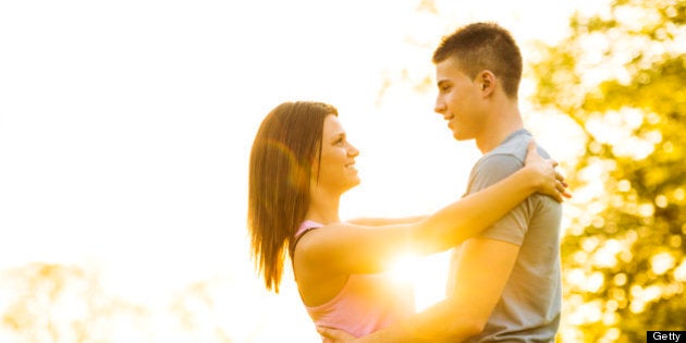 Embraced teenage couple standing and looking at each other surrounded by nature.