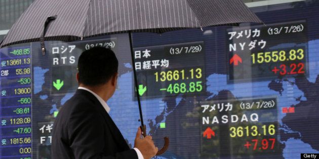 A pedestrian holding an umbrella looks at an electronic stock board displaying the closing figure of the Nikkei 225 Stock Average, top center, outside a securities firm in Tokyo, Japan, on Monday, July 29, 2013. Japan shares fell, with the Topix index capping the biggest two-day loss in two months, as exporters slumped on a stronger yen and Mitsubishi UFJ Financial Group Inc. and Sumitomo Mitsui Financial Group Inc. sparked banks' biggest back-to-back retreat since May. Photographer: Tomohiro Ohsumi/Bloomberg via Getty Images