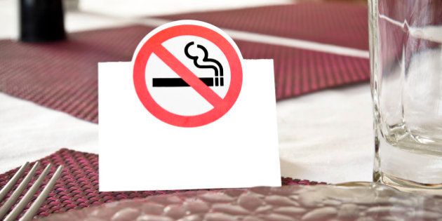 Close up of white no smoking sign displayed on a table in a public establishment (restaurant for example) with some cutlery visible. There is a white blank space to write 'No smoking' in the selected language.