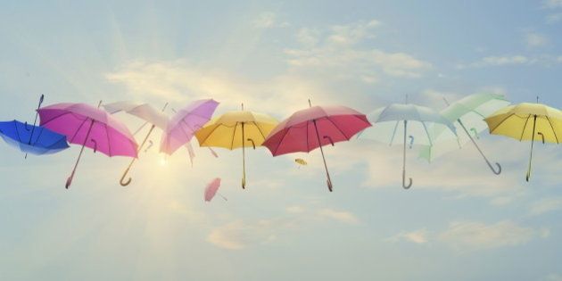 Conceptual photo of different color umbrellas lined-up across the sky. Sun is behind them shining, and this concept can represent team work, individuality, success of different people working together etc.