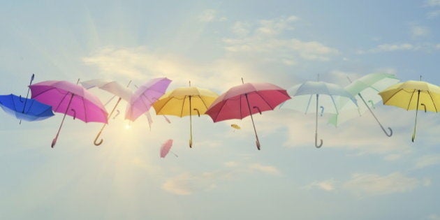 Conceptual photo of different color umbrellas lined-up across the sky. Sun is behind them shining, and this concept can represent team work, individuality, success of different people working together etc.