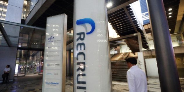 A man holding an umbrella walks past signage for Recruit Holdings Co. outside the building housing the company's head office in Tokyo, Japan, on Wednesday, Sept. 10, 2014. Recruit, a Japanese provider of staffing services, plans to raise about 178 billion yen ($1.7 billion) in an initial public offering next month to expand through acquisitions and investments. Photographer: Tomohiro Ohsumi/Bloomberg via Getty Images