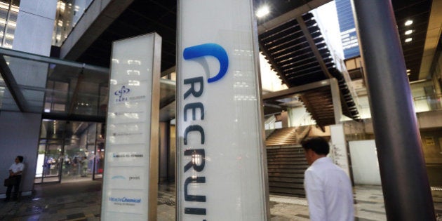 A man holding an umbrella walks past signage for Recruit Holdings Co. outside the building housing the company's head office in Tokyo, Japan, on Wednesday, Sept. 10, 2014. Recruit, a Japanese provider of staffing services, plans to raise about 178 billion yen ($1.7 billion) in an initial public offering next month to expand through acquisitions and investments. Photographer: Tomohiro Ohsumi/Bloomberg via Getty Images