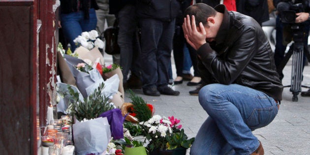 A man holds his head in his hands as he lays flowers in front of the Carillon cafe, in Paris, Saturday, Nov.14, 2015. French President Francois Hollande vowed to attack Islamic State without mercy as the jihadist group admitted responsibility Saturday for orchestrating the deadliest attacks inflicted on France since World War II. (AP Photo/Thibault Camus)