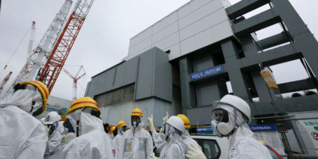 Members of the media and Tokyo Electric Power Co. (Tepco) employees wearing protective suits and masks stand in front of the building housing the No. 4 reactor at the Fukushima Dai-ichi nuclear power plant in Okuma, Fukushima Prefecture, Japan, on Thursday, Nov. 7, 2013. Tepco, which returned to profitability in its first-half earnings report on Oct. 31, is handling an estimated 11 trillion yen ($112 billion) cleanup of the nuclear plant wrecked by an earthquake and tsunami in 2011. Photographer: Kimimasa Mayama/Pool via Bloomberg