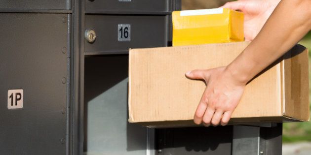 Horizontal image of female hands putting packages into postal mailbox with green grass and sidewalk in background