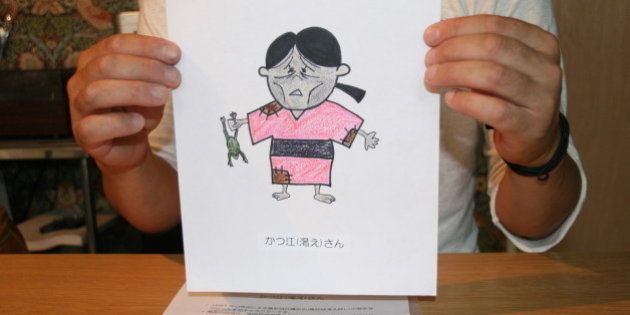 鳥取城跡のマスコットキャラクター「かつ江さん」のデザイン画を手にする発案者の男性