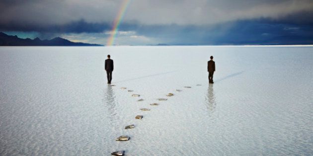 Two businessmen standing at the end of forked stone pathway in water with rainbow over one businessman