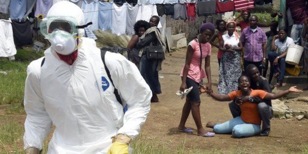 People look on as a woman reacts after her husband is suspected of dying from the Ebola virus, in the Liberian capital Monrovia, on October 4, 2014. By far the most deadly epidemic of Ebola on record has spread into five west African countries since the start of the year, infecting more than 7,000 people and killing about half of them. AFP PHOTO / PASCAL GUYOT. (Photo credit should read PASCAL GUYOT/AFP/Getty Images)
