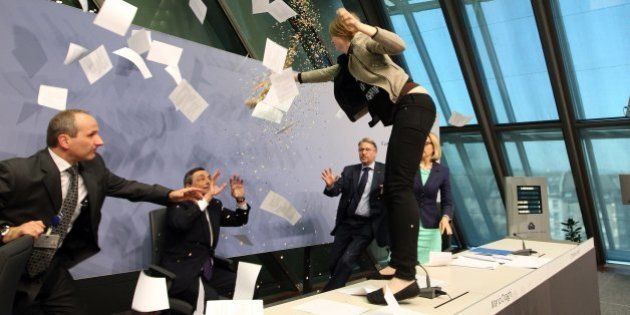 A woman interrupts a press conference by Mario Draghi (C), President of the European Central Bank, (ECB) following a meeting of the Governing Council in Frankfurt / Main, Germany, on April 15, 2015. AFP PHOTO / DANIEL ROLAND (Photo credit should read DANIEL ROLAND/AFP/Getty Images)