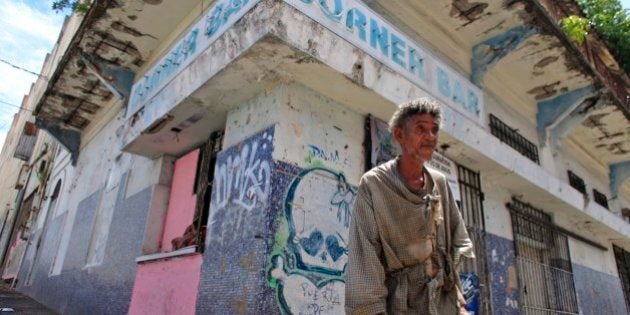 A homeless man stands in front of a closed down business in Puerta de Tierra in the outskirts of Old San Juan, Puerto Rico, Sunday, Aug. 2, 2015. Mired in a 10 year old economic crisis, Puerto Rico failed to pay a $58 million bond payment due Saturday. If defaults continue, analysts say Puerto Rico will face numerous lawsuits and increasingly limited access to markets, putting a recovery even more out of reach. (AP Photo/Ricardo Arduengo)