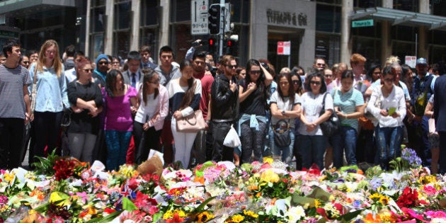 Staff members from the Lindt Chocolat Cafe with their arms linked pay tribute to their colleague who lost his live during a siege at the popular coffee shop at Martin Place in the central business district of Sydney, Australia, Tuesday, Dec. 16, 2014. The siege ended early Tuesday with a barrage of gunfire that left two hostages and the Iranian-born gunman dead, and a nation that has long prided itself on its peace rocked to its core. (AP Photo/Steve Christo)