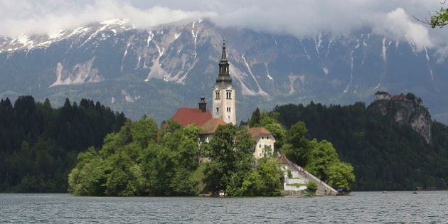 The church of the Assumption of Mary, a pilgrimage site and tourist attraction, is seen beneath the Julian Alps on Lake Bled, Slovenia, on Wednesday, May 8, 2013. Slovenia's recession will stretch into next year on weak domestic demand as the euro-area country teeters on the brink of needing an international bailout, the European Commission said. Photographer: Chris Ratcliffe/Bloomberg via Getty Images