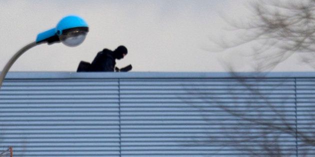 An armed police officer stands on the roof of a building in Dammartin-en-Goele, northeast of Paris, where the two brothers suspected in a deadly terror attack were cornered, Friday, Jan. 9, 2015. Two sets of attackers seized hostages and locked down hundreds of French security forces around the capital on Friday, sending the city into fear and turmoil for a third day in a series of linked attacks that began with the deadly newspaper terror attack that left 12 people dead. (AP Photo/Peter Dejong)