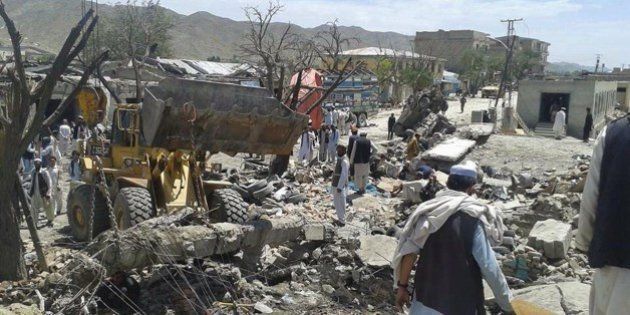 A loader removes debris as Afghans look on at the scene of a suicide attack at a market in Urgun district, Paktika province on July 15, 2014. A suicide bomber driving a truck packed with explosives killed at least 41 people at a busy market in southeastern Afghanistan on July 15, the deadliest attack in the war-torn country in months. The blast in Urgun in Paktika province highlights the fragile security situation Afghanistan faces as NATO withdraws its 50,000 combat troops, leaving local forces to contend with a resilient Taliban insurgency. AFP PHOTO/Khanazgul Farhang (Photo credit should read KHANAZGUL FARHANG/AFP/Getty Images)