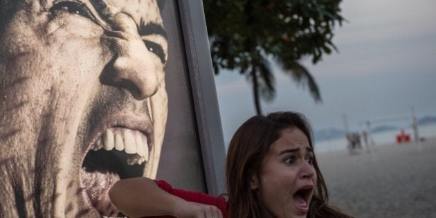 A tourist jokes in front of an advertisement with the portrait of Uruguay's forward Luis Suarez at Copacabana beach in Rio de Janeiro, Brazil, on June 26, 2014. Sportswear giant Adidas said Thursday it would stop using Luis Suarez, one of its key promotional stars, for World Cup adverts after his four-month ban from football activities for biting Italian Giorgio Chiellini. AFP PHOTO / YASUYOSHI CHIBA (Photo credit should read YASUYOSHI CHIBA/AFP/Getty Images)