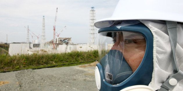 A member of the media, wearing a protective suit and a mask, stands in front of Tokyo Electric Power Co.'s (Tepco) Fukushima Dai-Ichi nuclear power plant in Okuma Town, Fukushima Prefecture, Japan, on Saturday, May 26, 2012. Japan, once the world's largest user of nuclear power after the U.S. and France, has all of its 50 reactors offline as the country runs safety tests following the Fukushima atomic disaster. Photographer: Tomohiro Ohsumi/Bloomberg via Getty Images
